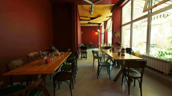 A restaurant with wooden tables and chairs, large windows, and a red wall. - Hotel Alabin Central (Sofia)