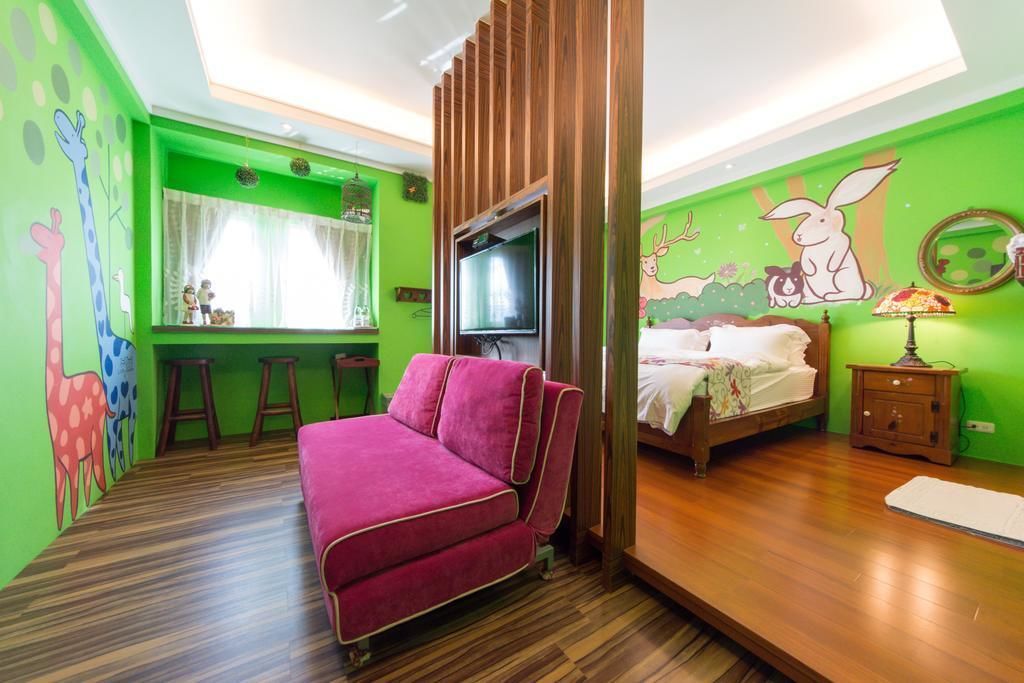 Una habitación con cama, sofá, televisor y pared verde decorada con murales de animales.