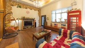 A living room with a stone wall, a fireplace, a television, a red telephone booth, and a striped sofa. - British Country Inn B&B (Luodong)