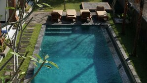 Ein rechteckiger Pool mit klarem, blauem Wasser, umgeben von einer Steingrenze. Am Pool befinden sich mehrere Liegestühle und ein Tisch.