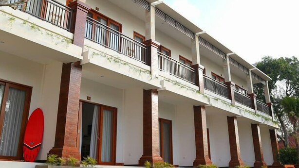 A multi-story hotel with balconies, large windows, and a red surfboard on the ground floor. - Seno Guesthouse & Cafe (Pecatu)