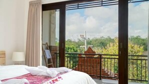 A hotel room with a bed, a balcony with a view of greenery, and a window with curtains. - Seno Guesthouse & Cafe (Pecatu)