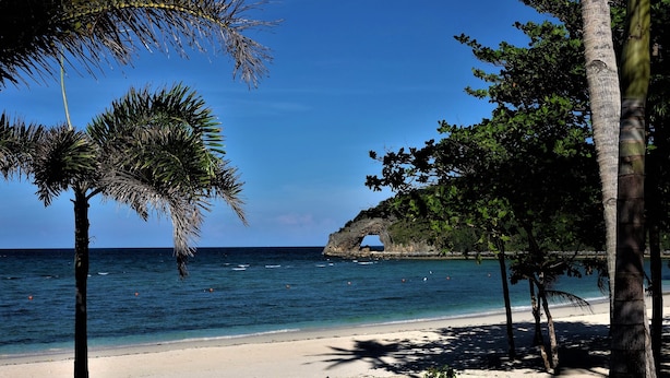 A beach with clear blue water, palm trees, and a rock formation. - Gerbi's Condoplace at Oceanway Residences Boracay (Boracay Island)