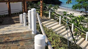 A stone pathway leading to a wooden pergola overlooking a beach with white bollards and a rope barrier. - Gerbi's Condoplace at Oceanway Residences Boracay (Boracay Island)