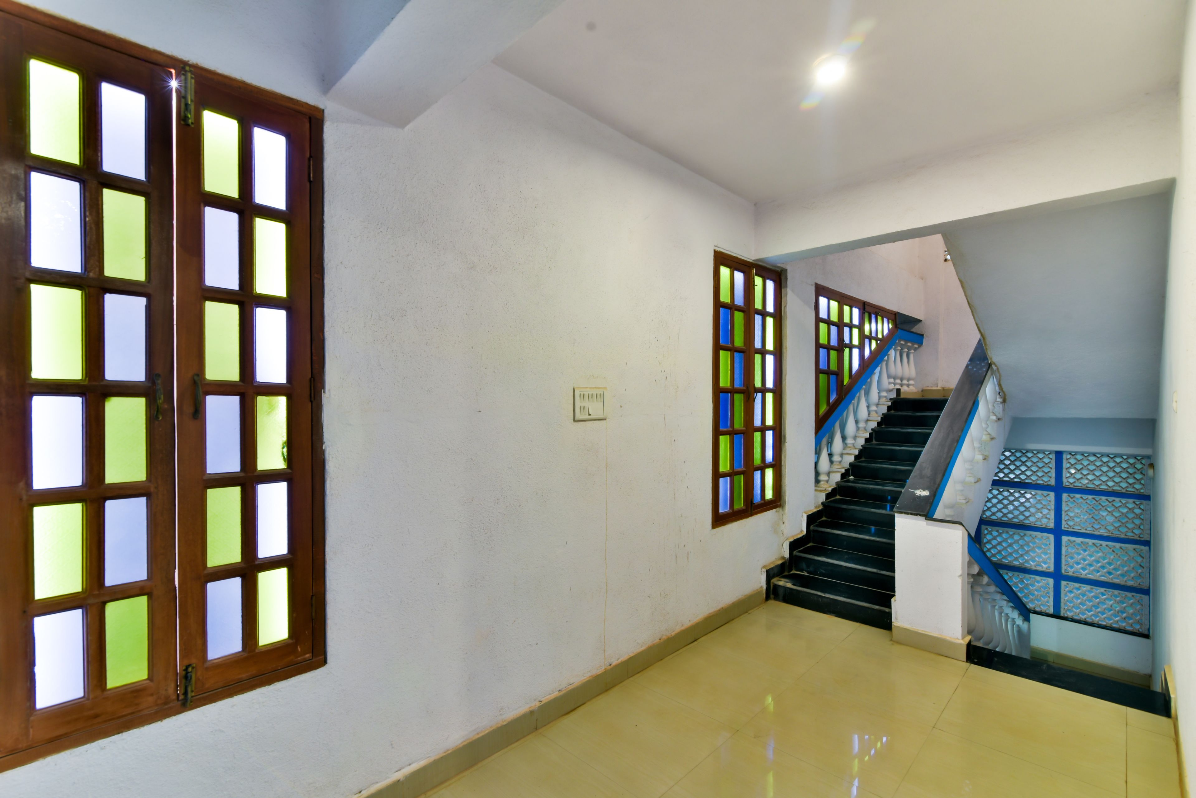 A hallway with a staircase, a door with glass panels, and a light switch on the wall.