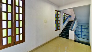 A hallway with a staircase, a door with glass panels, and a light switch on the wall. - Baga Fantacia Beach Inn (Baga)