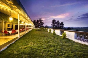 Un área de estar al aire libre con techo, mesas y sillas, un césped y vistas del paisaje.