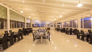 A spacious dining area with multiple tables and chairs, large windows, and a high ceiling with hanging lights. - GP Farm (Nashik)