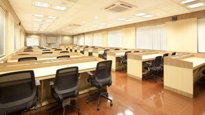 A conference room with multiple rows of desks and chairs, large windows with blinds, and a projector screen on the far wall. - GP Farm (Nashik)