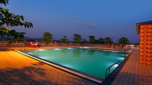 A rectangular swimming pool with a tiled deck, surrounded by a fence and trees. - GP Farm (Nashik)
