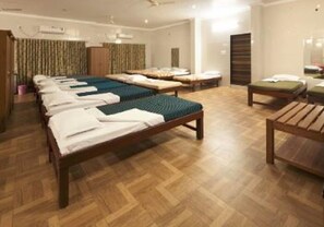 A hotel room with multiple beds arranged in a row, wooden flooring, and a large mirror on one wall. - GP Farm (Nashik)