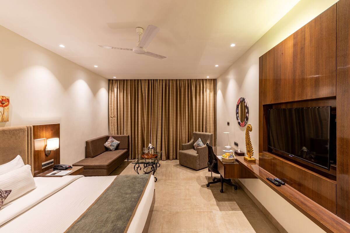 A hotel room with a bed, a desk, a chair, a TV, and a ceiling fan.