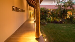 Un pasillo con techo de madera, cuadros en la pared y un jardín bien iluminado con palmeras.