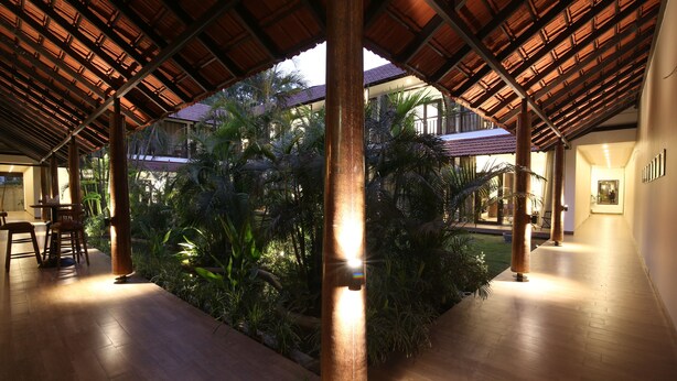 Un espacio interior con piso de madera, una columna central y una zona cubierta con plantas.