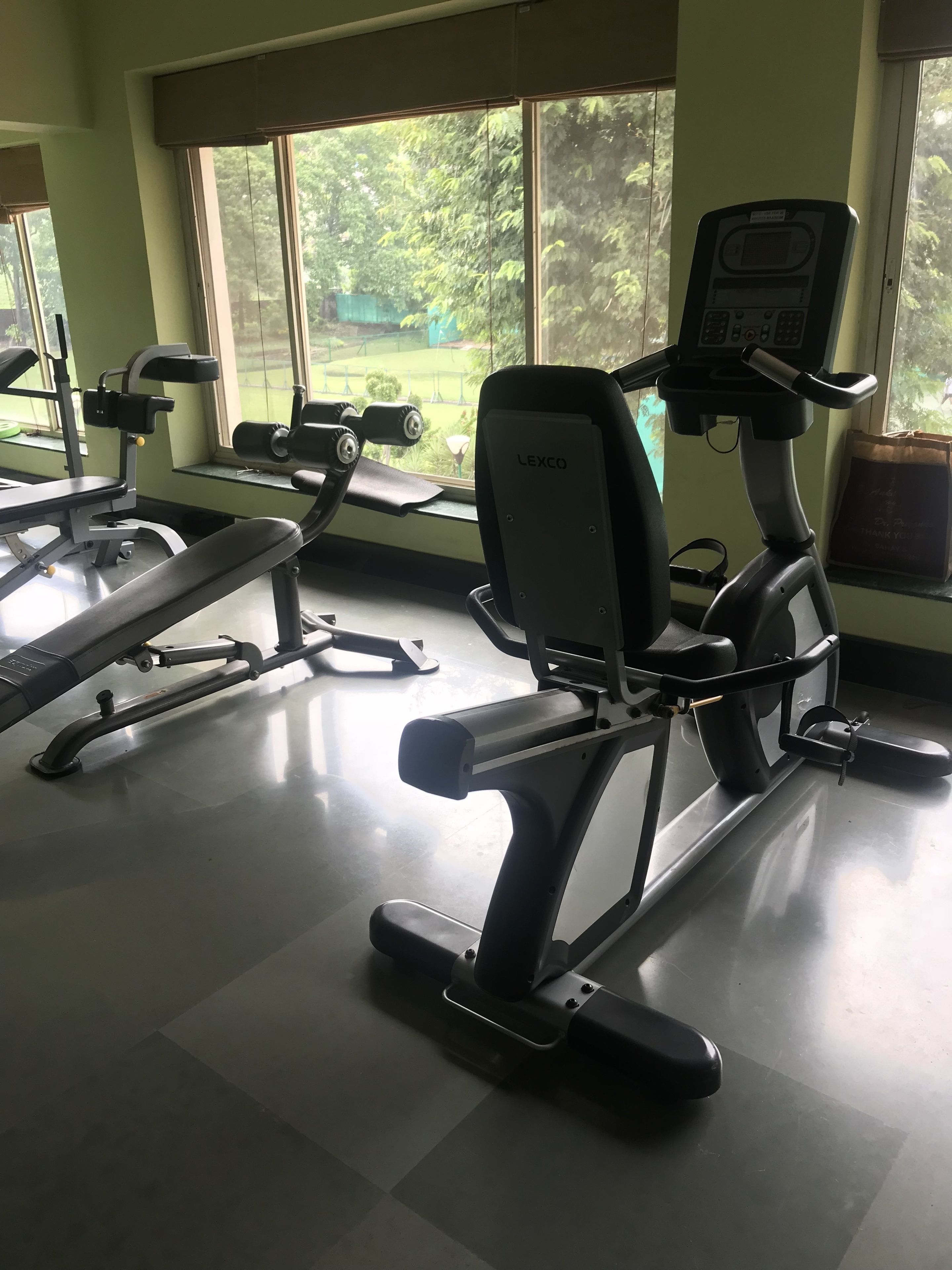 A gym with exercise equipment, large windows, and a view of greenery outside.