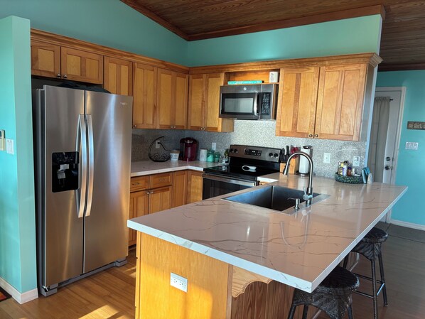A modern kitchen with wooden cabinets, stainless steel appliances, a granite countertop, and a built-in island with bar stools. - Stunning sea views as seen on HGTV’s Bahamas Life! (Exuma)