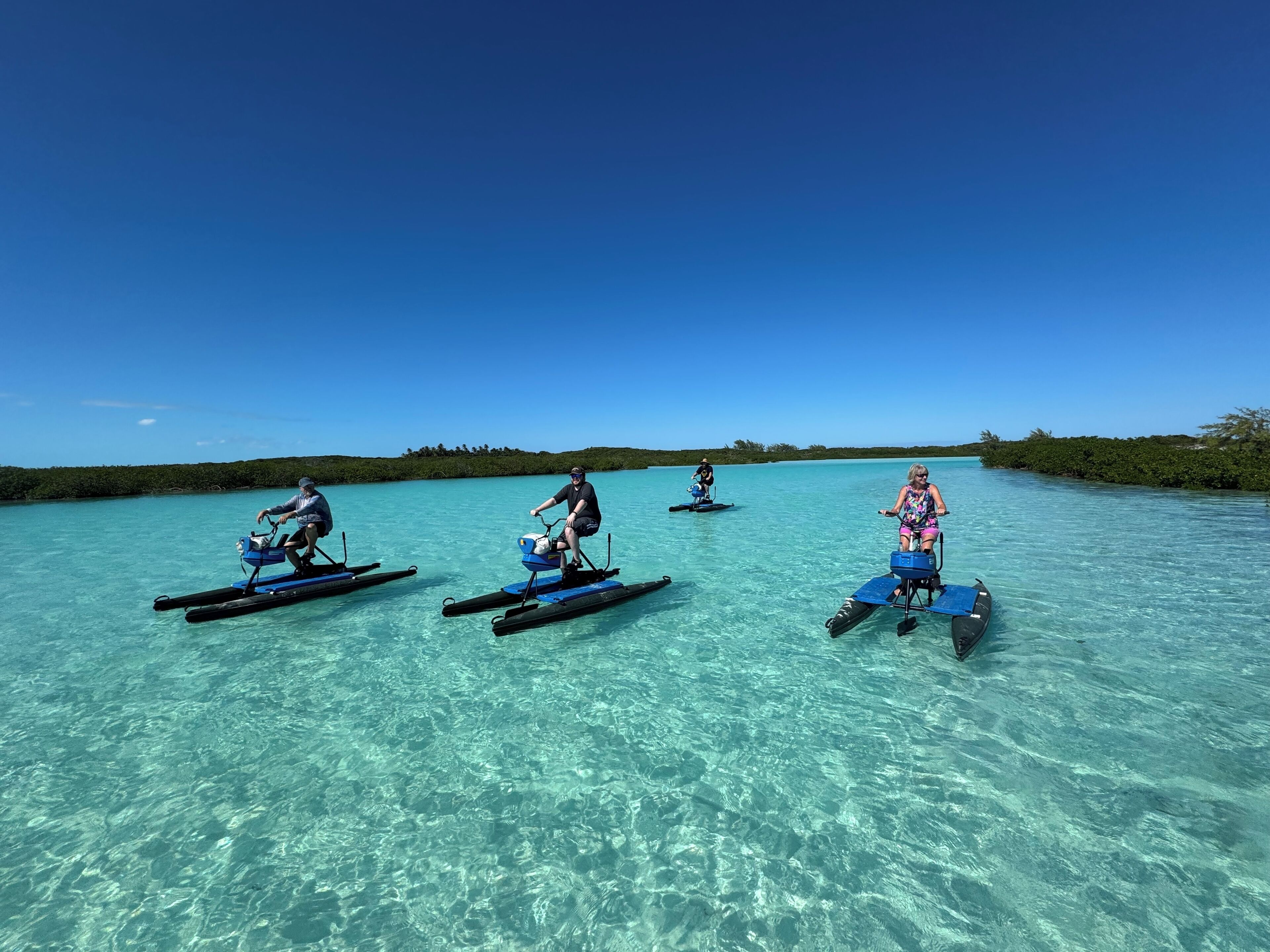 Drie mensen op waterfietsen in helder, turquoise water.