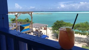 Vista desde un balcón con vista a una playa y aguas turquesas cristalinas, con una isla a lo lejos.
