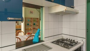 Een keuken met een gasfornuis, een spoelbak en een raam dat uitkomt op een eetgedeelte met een tafel en stoelen.