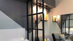 A modern hotel room with a large bed, two armchairs, a sofa, and a partition with hooks.