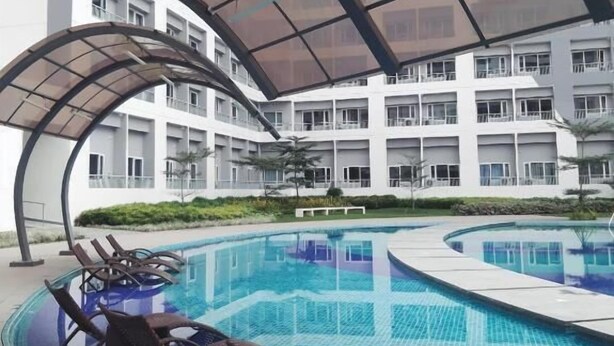 A swimming pool with lounge chairs and a covered area, surrounded by a modern building with multiple balconies.