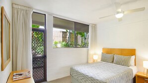 Een hotelkamer met een bed, nachtkastjes, een plafondventilator en een raam met uitzicht op groen.