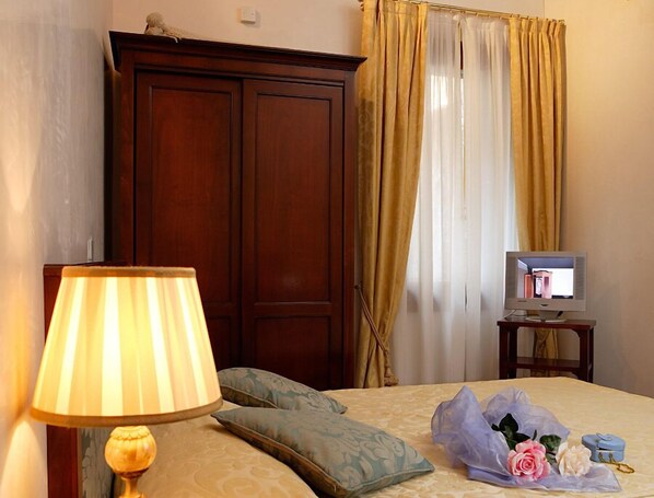 A hotel room with a bed, a lamp, a television on a side table, and a wardrobe.