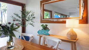 Un comedor con mesa de madera, sillas, un florero con flores, una lámpara, un espejo y un cartel que dice 'BEACH'.