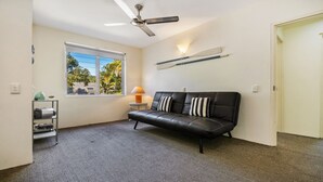 Een moderne woonkamer met een leren bank in zwart, een plafondventilator, een groot raam met uitzicht op groen en een vloerbedekking.