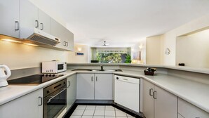 Een moderne keuken met witte kastjes, een magnetron, fornuis, oven en een raam met uitzicht op groen.