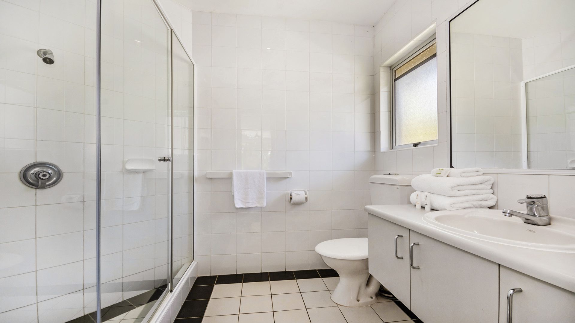 Un bagno moderno con box doccia in vetro, un water, un lavandino con specchio e asciugamani ordinatamente riposti.