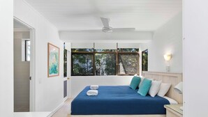 Quarto com cama, mesa de cabeceira, janela com vista para árvores e ventilador de teto.