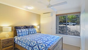 A bedroom with a bed, nightstands, a ceiling fan, and a window with blinds. - Ludlow Apartments (Noosa Heads)