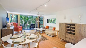 A modern living room with a dining area, a sofa, a TV, and a wine rack. - Ludlow Apartments (Noosa Heads)