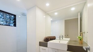 A modern bathroom with a large mirror, white cabinets, and a brown countertop. - Ludlow Apartments (Noosa Heads)