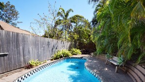A swimming pool with a checkered edge, surrounded by a wooden fence and lush greenery. - Ludlow Apartments (Noosa Heads)