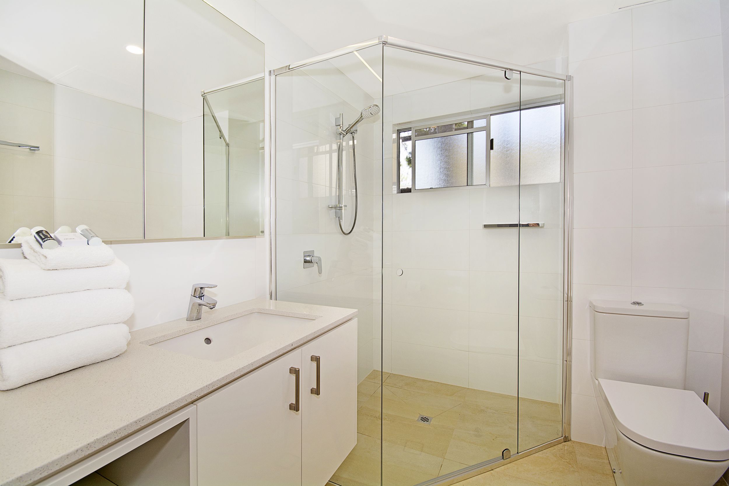 Ein modernes Badezimmer mit einer gläsernen Dusche, einem weißen Waschbecken mit Spiegel darüber und einer Toilette.