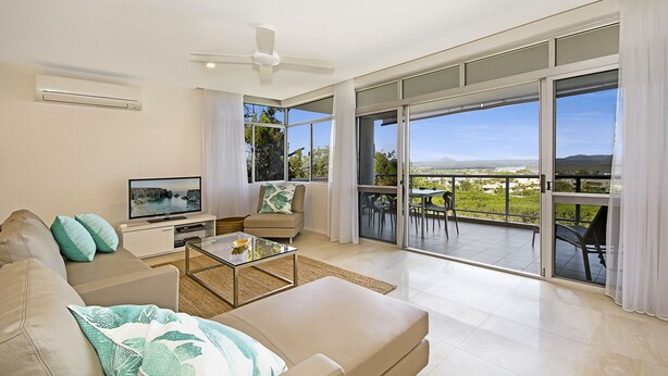 A modern living room with a sofa, coffee table, and TV, leading to a balcony with a view of the landscape. - Outlook (Noosa Heads)