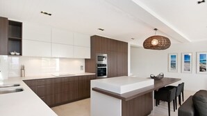 A modern kitchen with a central island, dark wooden cabinets, and a white countertop. - Outlook (Noosa Heads)
