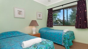 A room with two beds, a nightstand, a lamp, and a window with curtains.