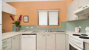 A compact kitchen with a dishwasher, stove, and a window with blinds.