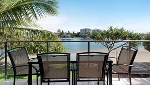 A balcony with a table and chairs overlooking a pool and buildings.