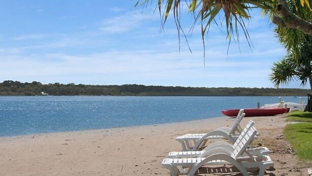 A beach with white lounge chairs and a red boat on the shore.