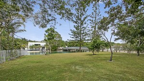 A grassy outdoor area with a bridge, trees, and a building in the background. - Kananda (Noosa Heads)