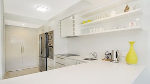 A modern kitchen with white cabinetry, stainless steel appliances, and a yellow vase on the counter. - Kananda (Noosa Heads)