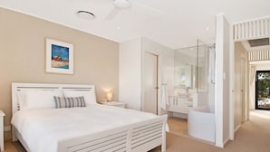 A modern bedroom with a large bed, a bedside table, a glass-enclosed shower, and a view of the outdoors. - Weyba Quays (Noosa Heads)