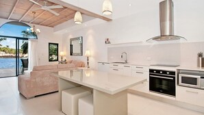 A modern kitchen with a central island, white cabinetry, stainless steel appliances, and pendant lighting. - Weyba Quays (Noosa Heads)