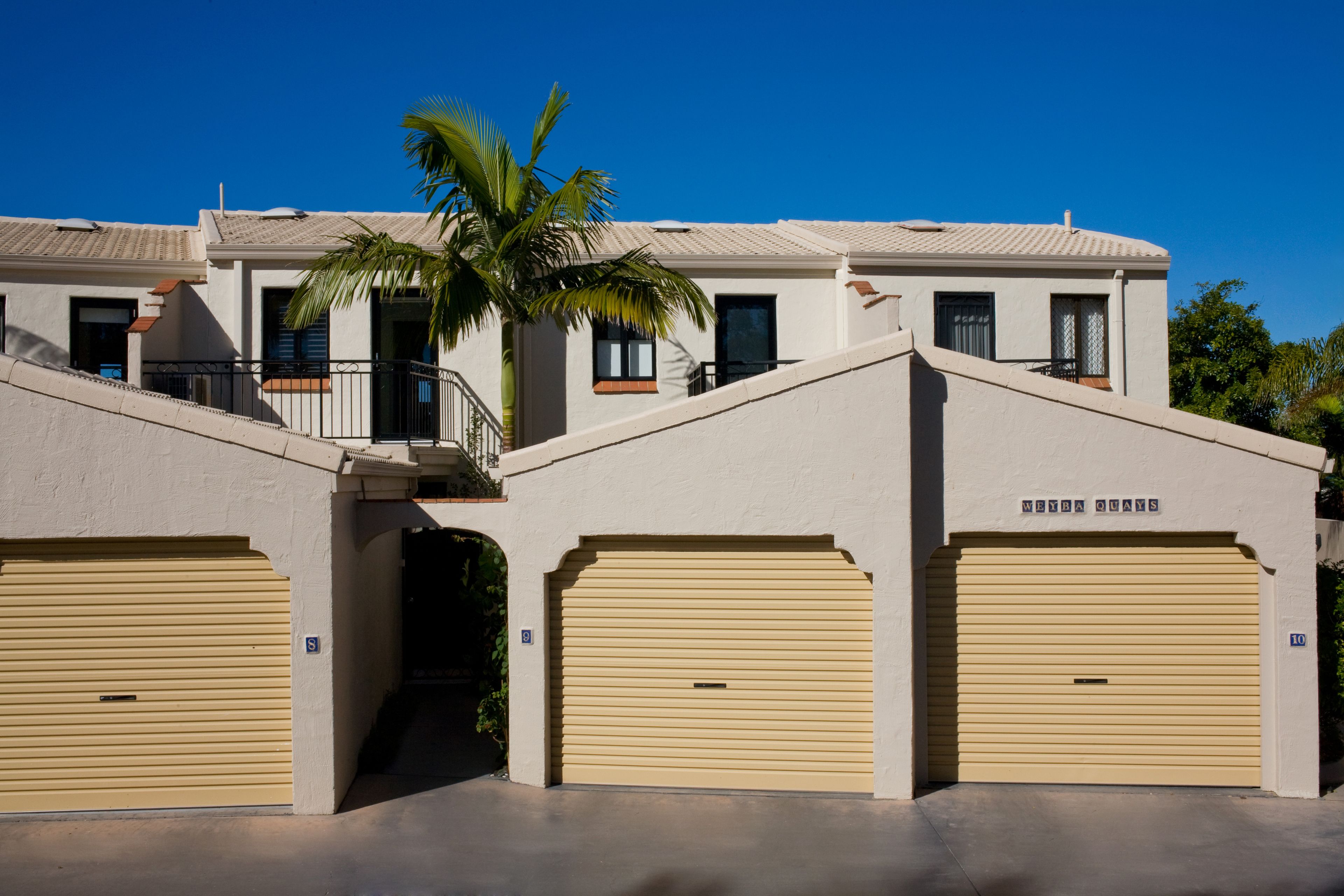 Un edificio con due porte per garage, una palma e un cielo azzurro limpido.