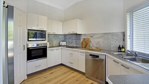 Eine moderne Küche mit weißen Schränken, einem Edelstahl-Kühlschrank, einem Backofen, einem Toaster, einem Geschirrspüler und einer Arbeitsplatte aus Granit.