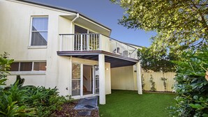 Ein zweistöckiges Haus mit Balkon, ein kleiner Vorgarten mit künstlichem Rasen und ein Holzzaun im Hintergrund.